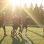 Seven high school football athletes run outdoors with rays of sunlight obscuring them into dark silhouettes.