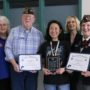 Alice Yang stands with 5 members of the VFW and the WSD superintendent with 2 awards and a plaque in hand