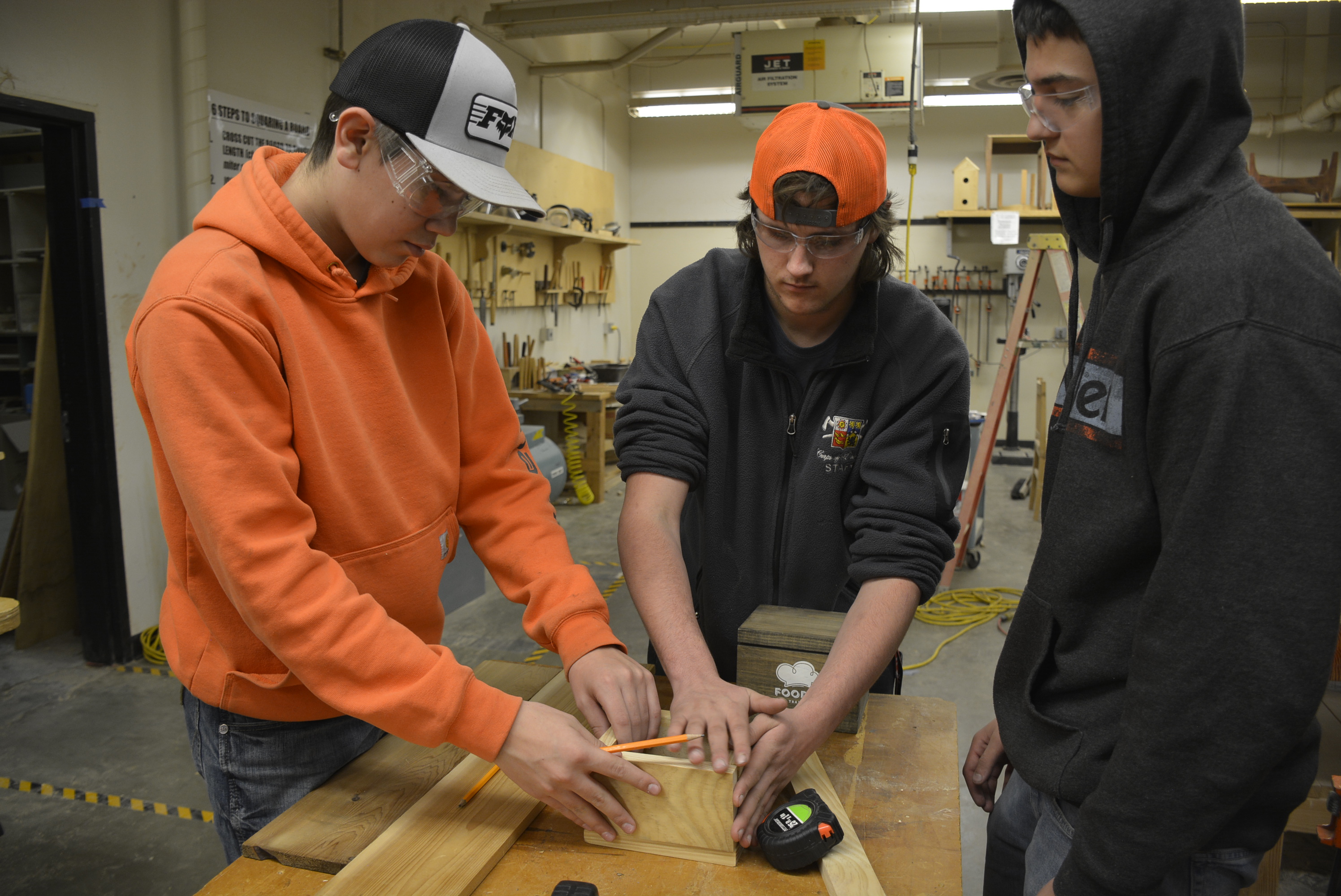 Three students working on a wooden box in the wood shop at a table