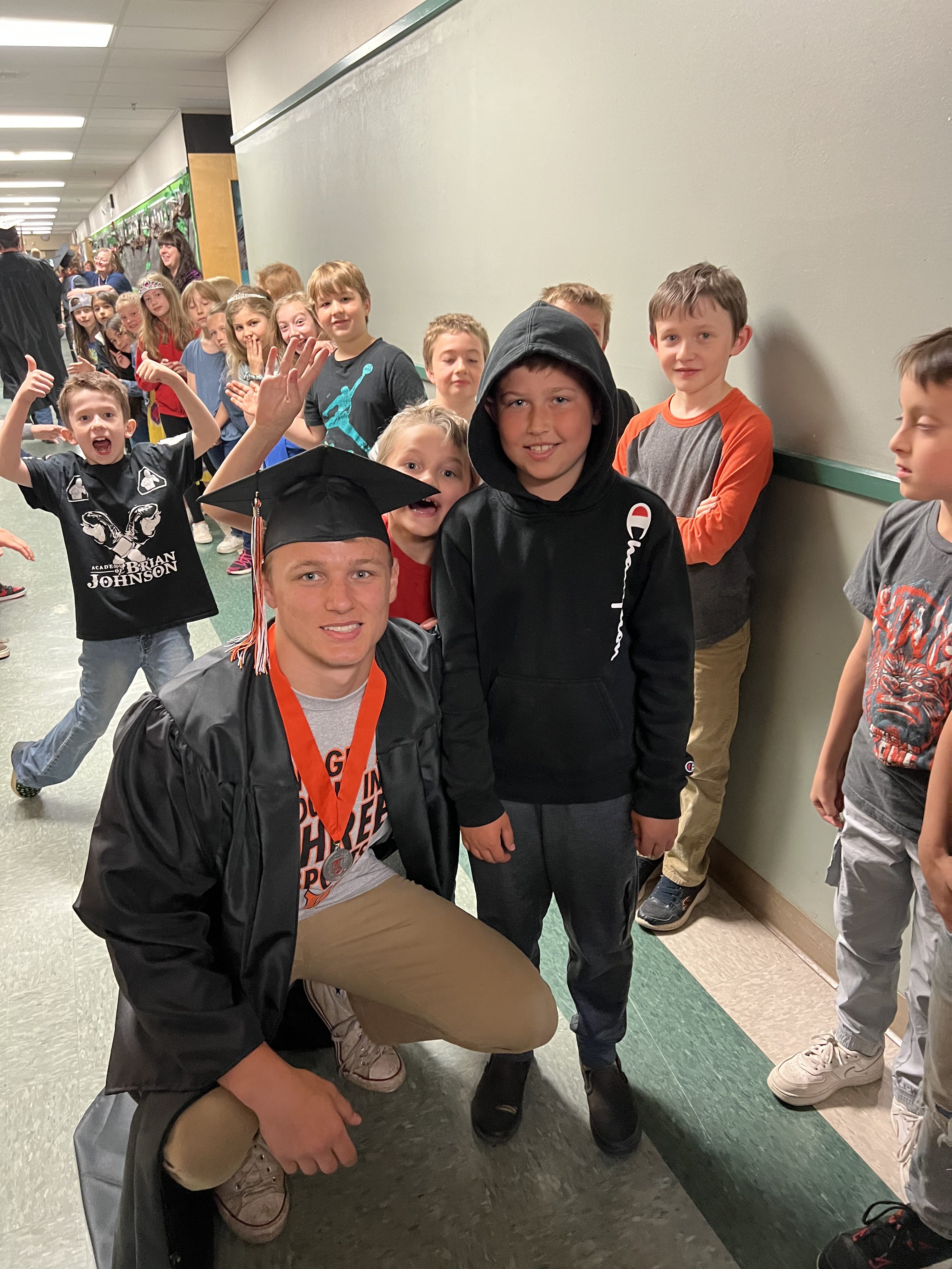 Graduate poses with younger students in hallway