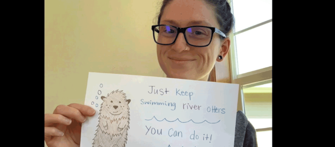 Staff member with sign saying Just keep Swimming Otters, you can do it