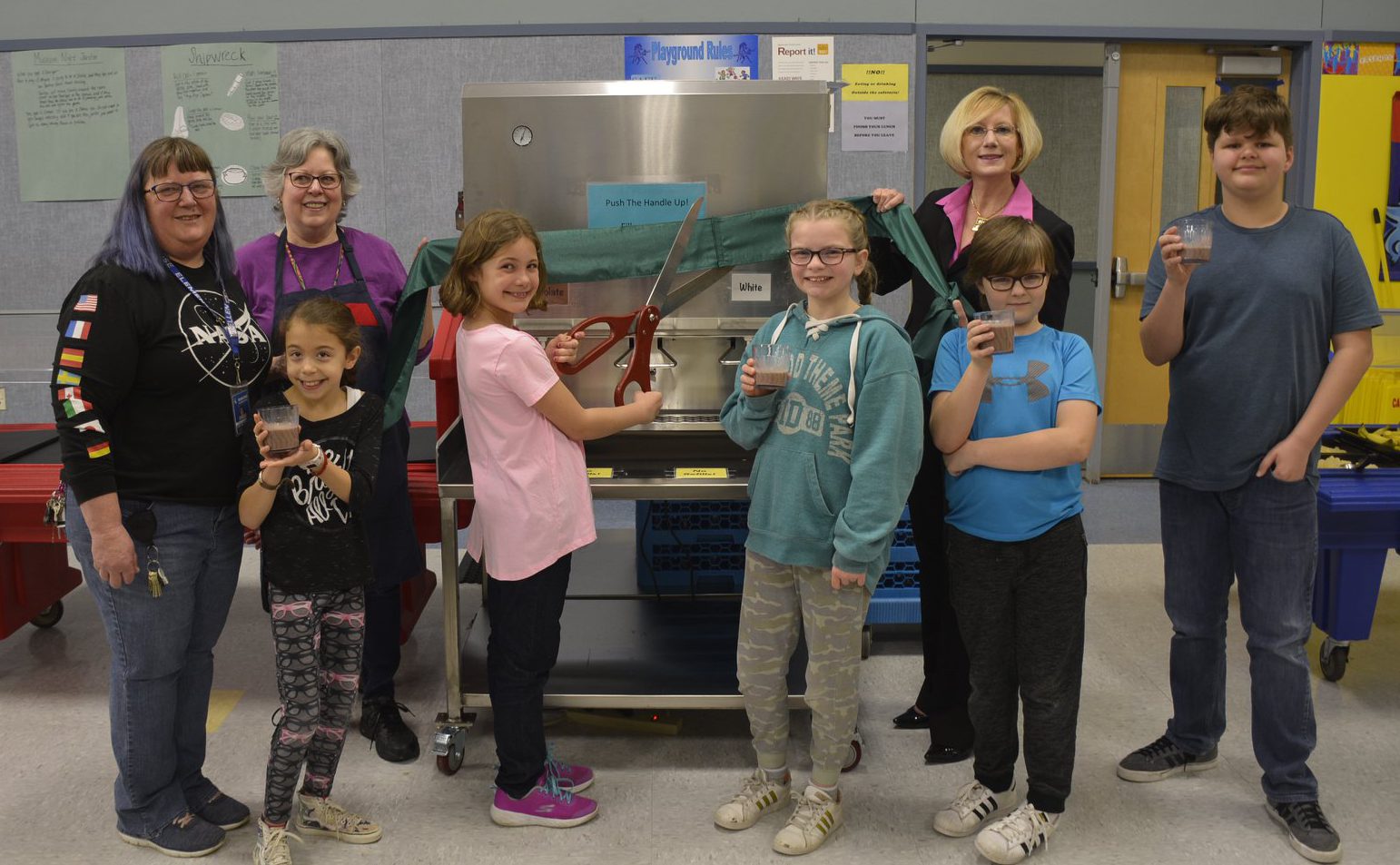 Members of the Gause Green Team, food service team, and students welcome the new milk dispenser to the school cafeteria, posing with cups of regular or chocolate milk.