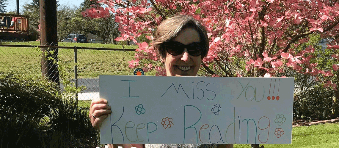 Gause staff member with sign that says "I miss you, keep reading"