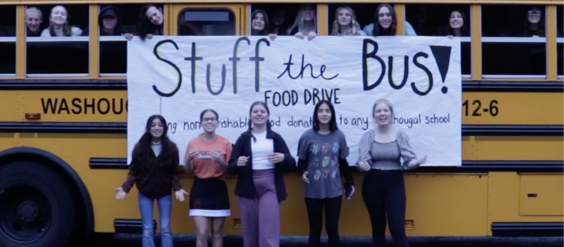 Students in front of School bus with banner saying Stuff the Bus Food Drive