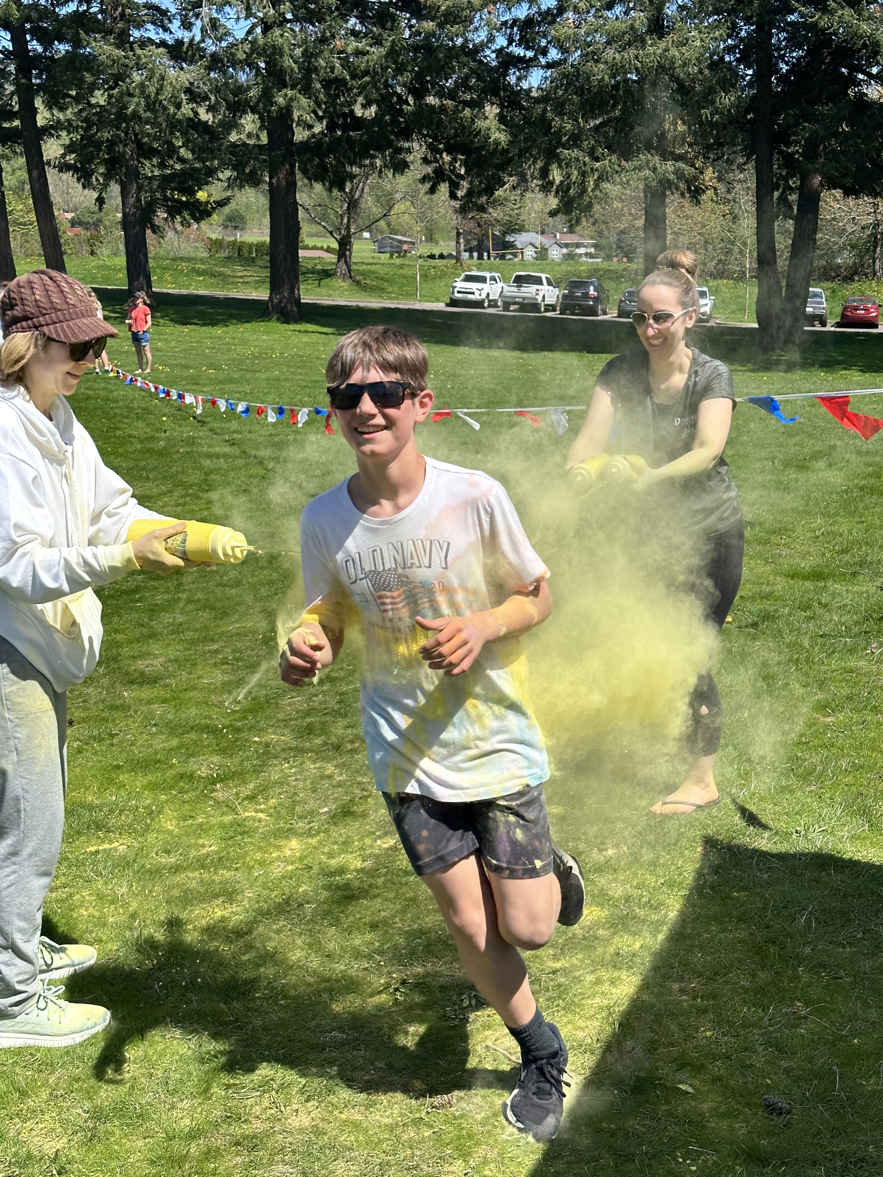 Student runs through two volunteers who spray them with yellow food safe dye