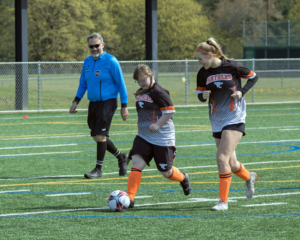 WHS Unified teammates Suzanne and Anna dribble the soccer ball with a referee in the background