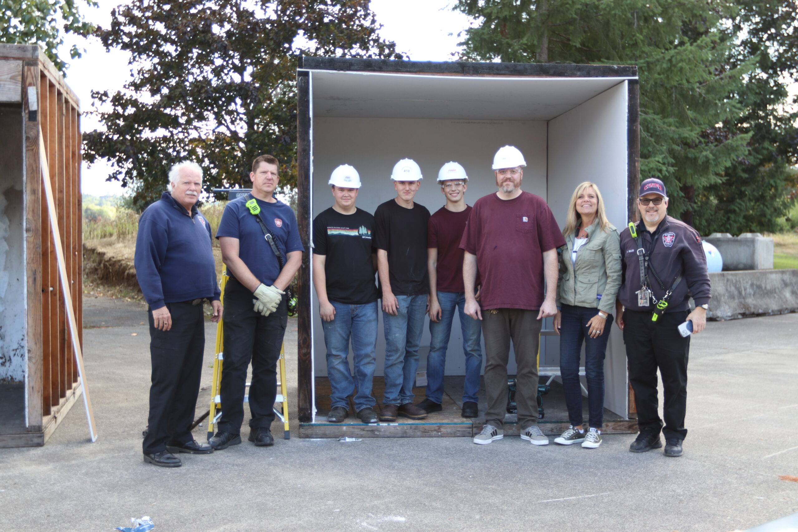 Students and fire fighters pose in front of rooms built to demonstrate fire safety