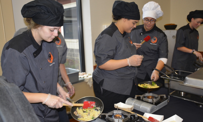 WHS Culinary students cooking pasta on a table in commons, and putting it onto plates
