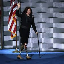 Senator Tammy Duckworth walking on stage with American flag in background
