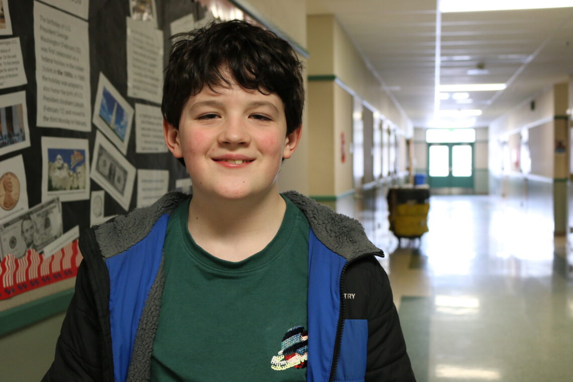 Boy stands in hallway and smiles at the camera