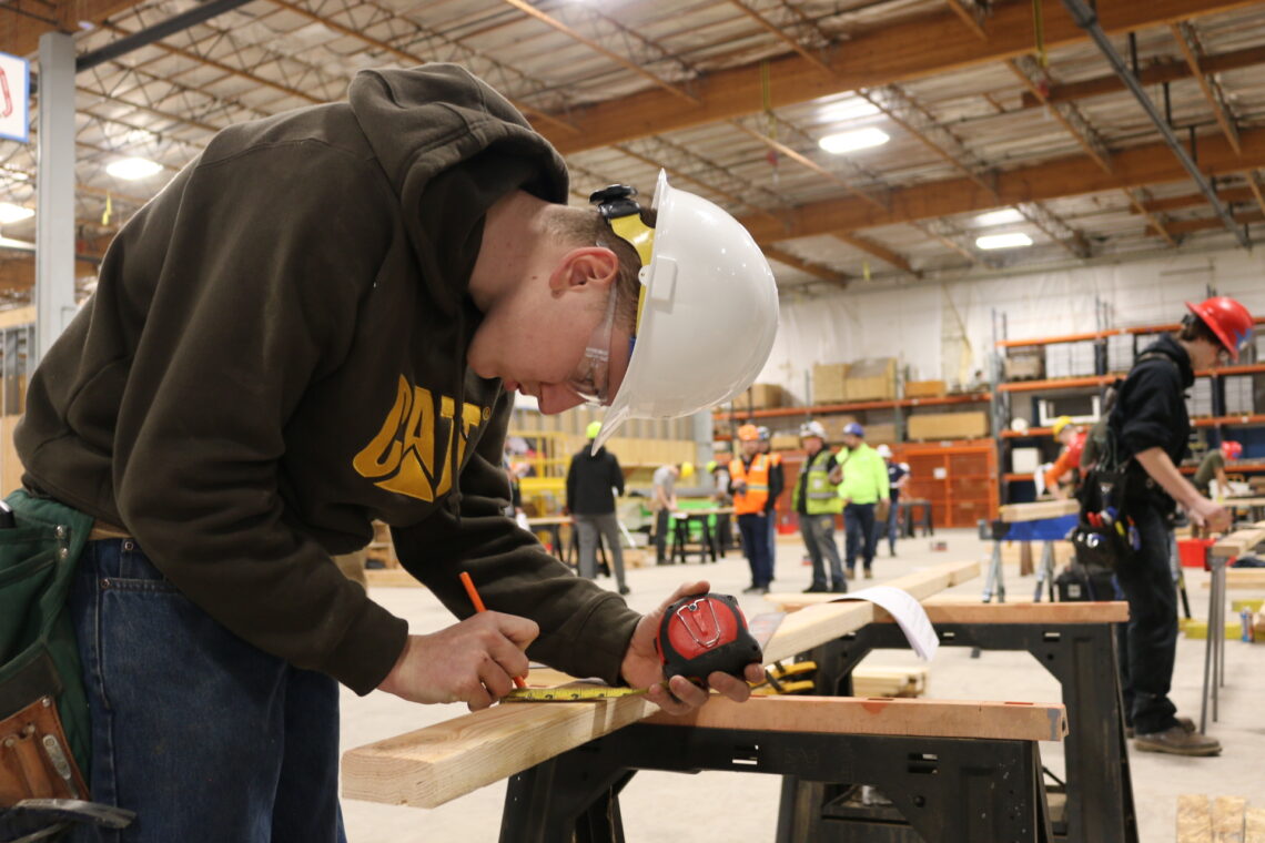 Student uses tape measure to mark 2x4 during construction competition