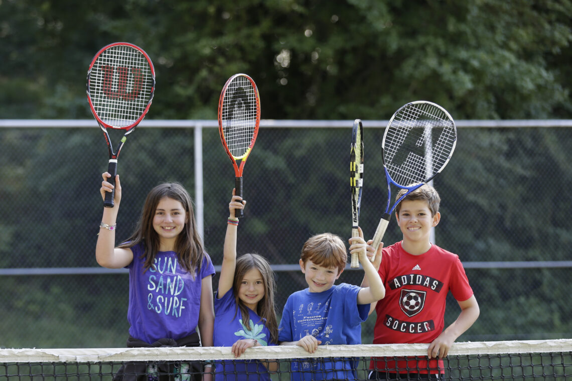 Students with tennis rackets behind net